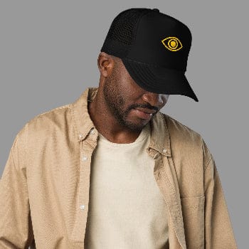 Man wearing a black cap with a yellow logo and a beige jacket on a white background