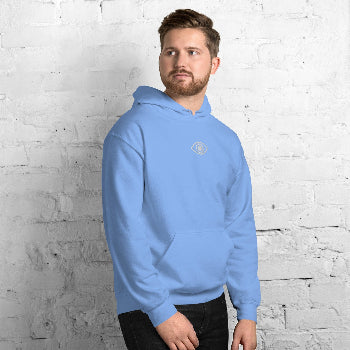 Man wearing a light blue hoodie with an eye logo against a white brick wall.