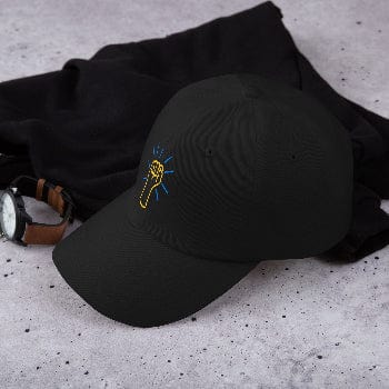 Black cap with a yellow and blue logo on a gray surface with black fabric and watch.