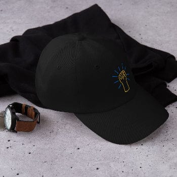 Black cap with embroidered design on a gray surface with a watch beside it