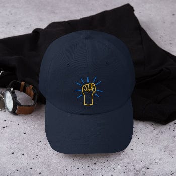 Navy blue cap with a yellow fist symbol on a gray surface with black fabric and watch.