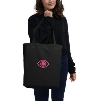 Person holding a black tote bag with a pink eye symbol on a white background