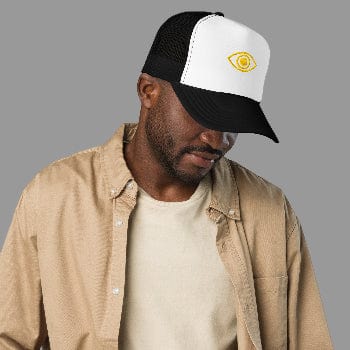Man wearing a black and white cap with a logo, beige jacket, and white shirt on a white background