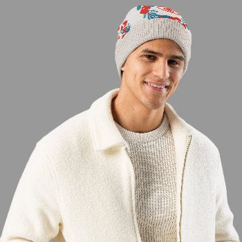 Man wearing a white knit beanie with floral patterns and a cream-colored jacket on a white background