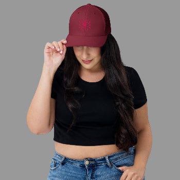 Woman wearing a maroon cap with a design, black crop top, and blue jeans on a white background