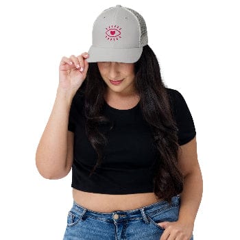 Woman wearing a black crop top and blue jeans, holding a gray cap with a red design.