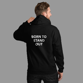 Person wearing a black hoodie with 'BORN TO STAND OUT' text on the back against a white brick wall.