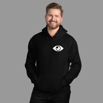Man wearing a black hoodie with a white eye logo against a white brick wall.