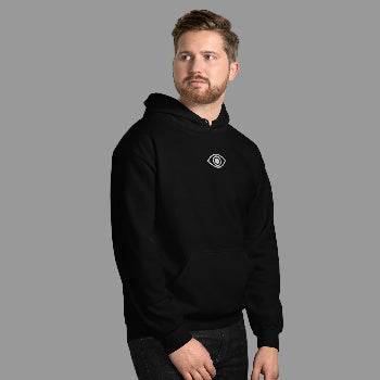 Man wearing a black hoodie with a logo against a white brick wall