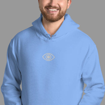Man wearing a light blue hoodie with an eye logo against a gray brick wall.