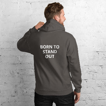 Man wearing a gray hoodie with 'BORN TO STAND OUT' text on the back against a white brick wall.