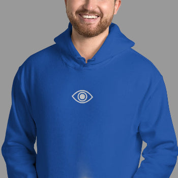 Man wearing a blue hoodie with an eye logo against a white brick wall.